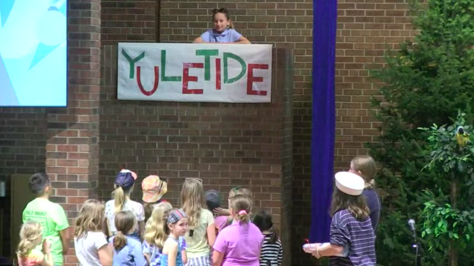 Children performing play at Nativity Lutheran Church. One child talking to others with banner that says "yuletide."