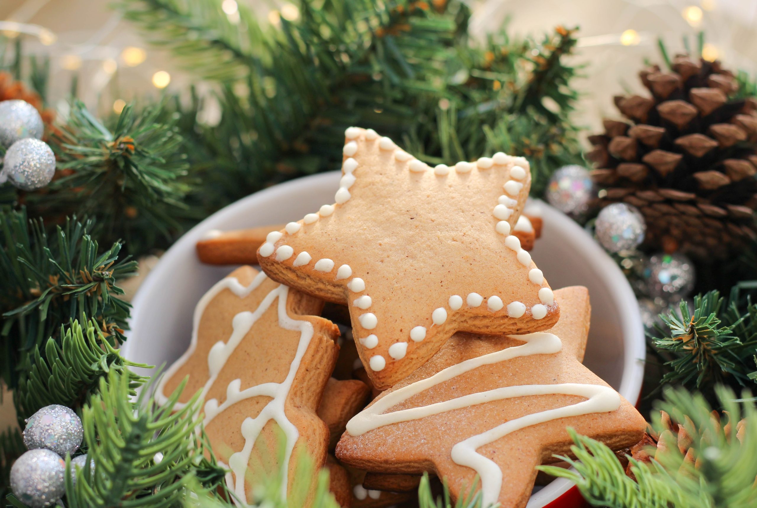 Christmas cookies in a bowl surrounded by Christmas greens, pinecones and silver decorations