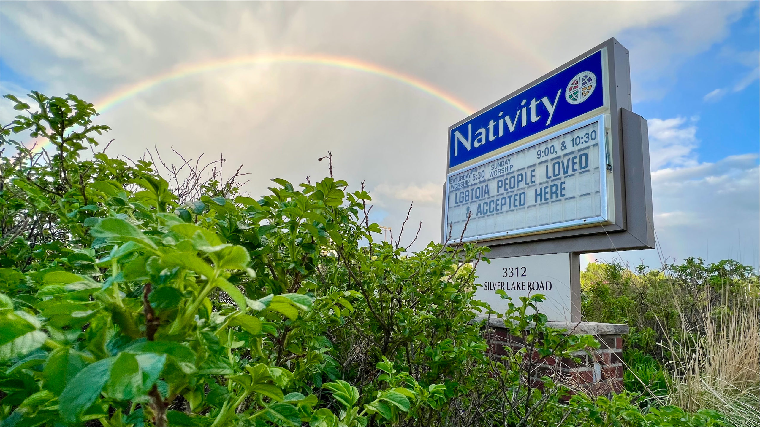 A rainbow in the sky goes over the Nativity Lutheran Church sign that says LGBTQIA people loved and accepted here