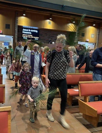Families walking down the Nativity sanctuary aisle with palms