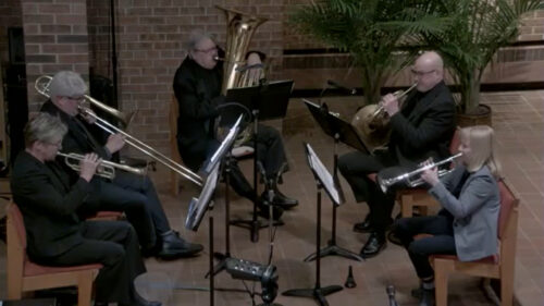 Five brass musicians of North Shore Brass seated playing brass instruments: 2 trumpets, one French horn, one trombone, one tuba
