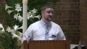 Mark Blaede preaching at Nativity Lutheran Church with lilies behind him