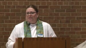 Pastor Angela LaMoore preaching in Nativity sanctuary with dark brick background