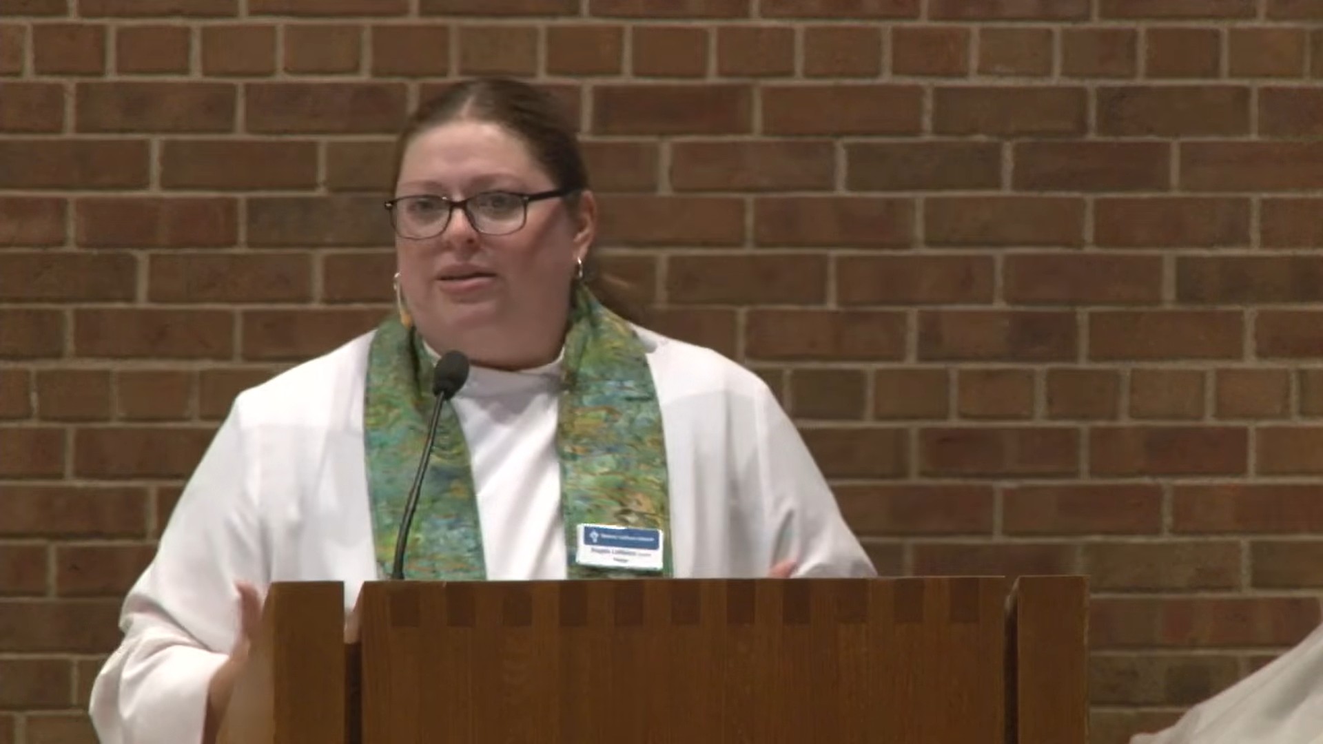 Pastor Angela LaMoore preaching in Nativity sanctuary with dark brick background