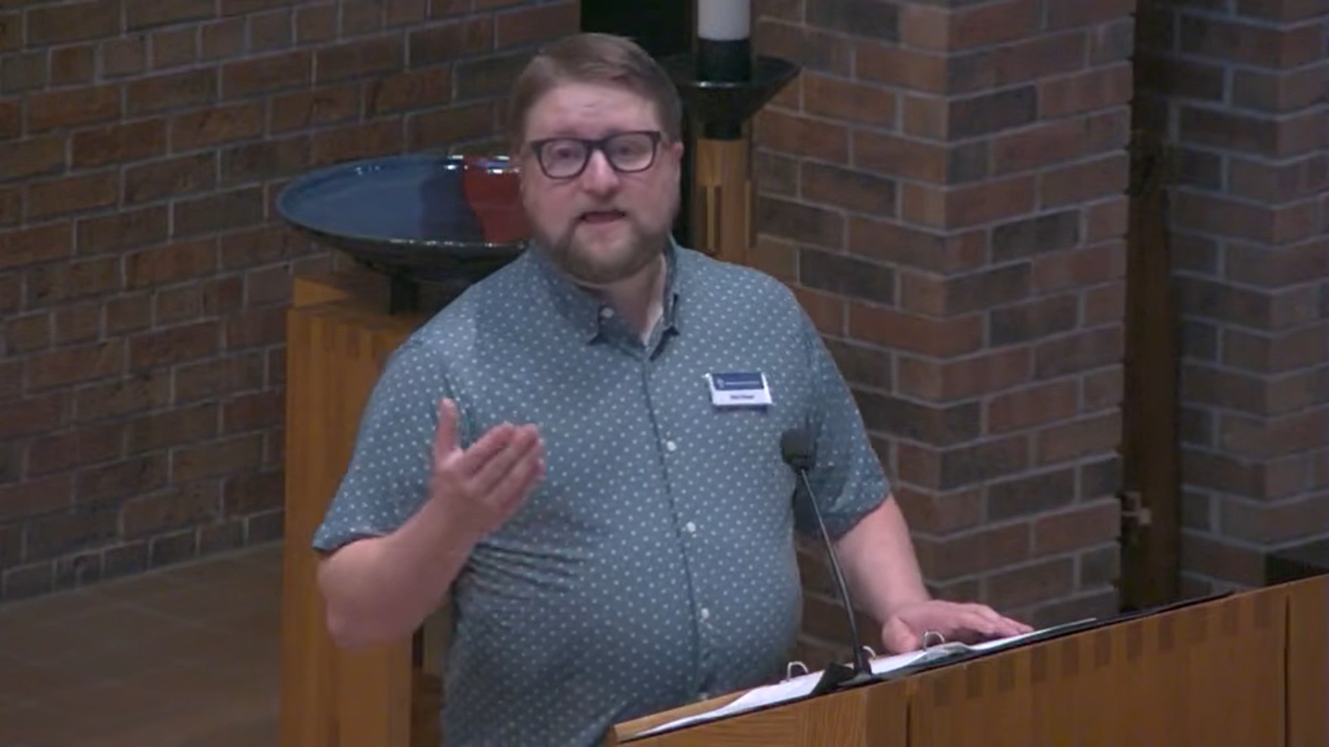 Mark Blaede preaching in the Nativity sanctuary with red brick background